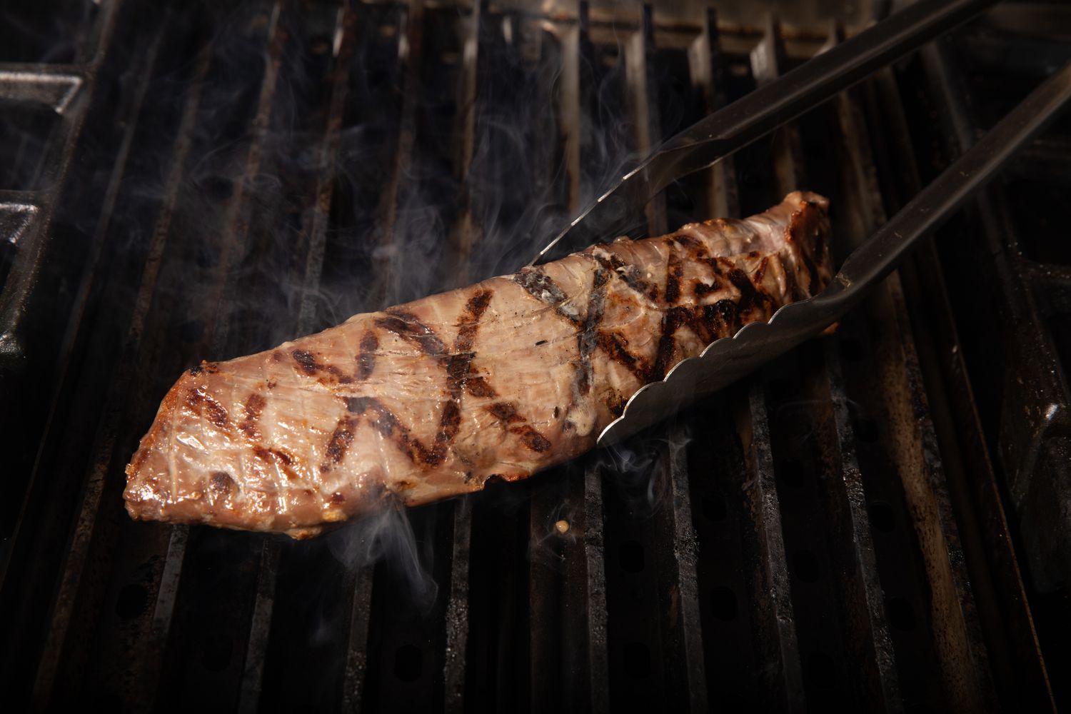 pork tenderloin on the grill as it's being rotated with tongs