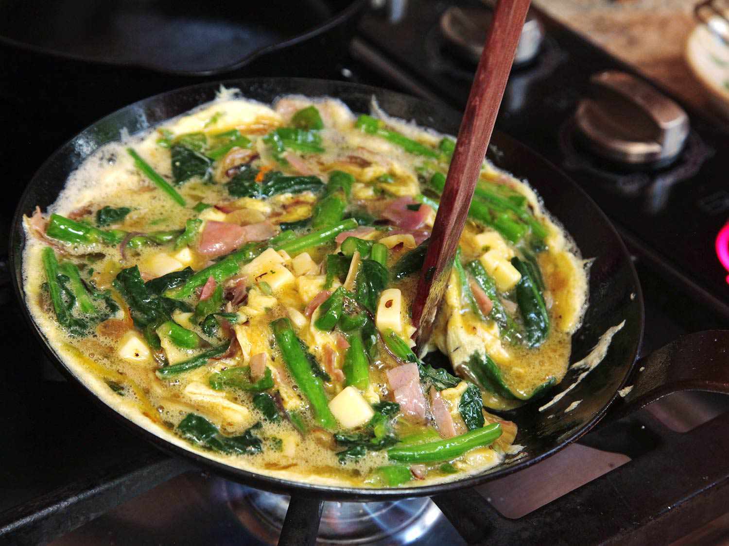 The half, cooked mixture is stirred with a wooden spoon.