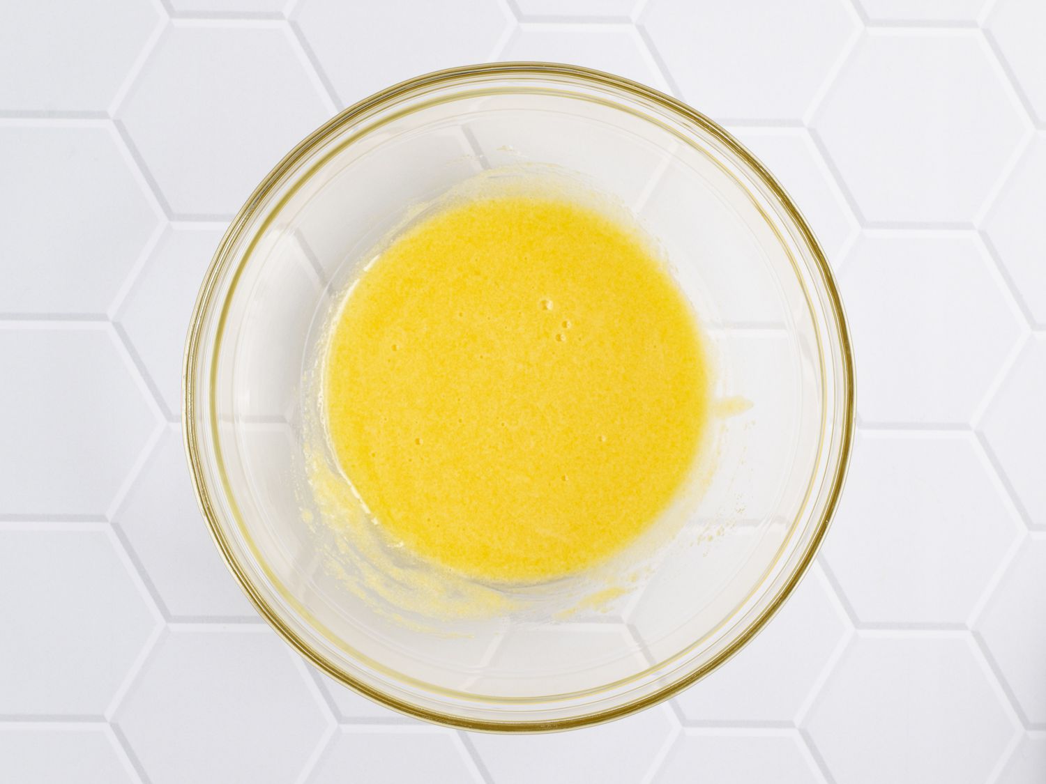 A glass bowl holding lightly beaten egg yolks and sugar.