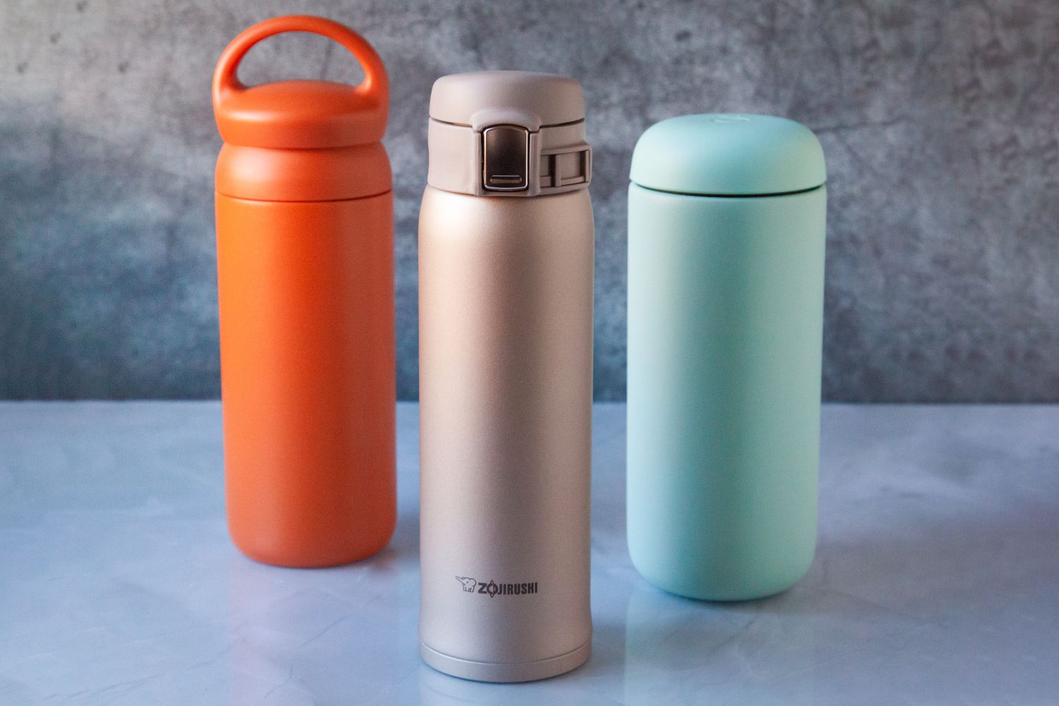 Three multicolored travel mugs on a surface.