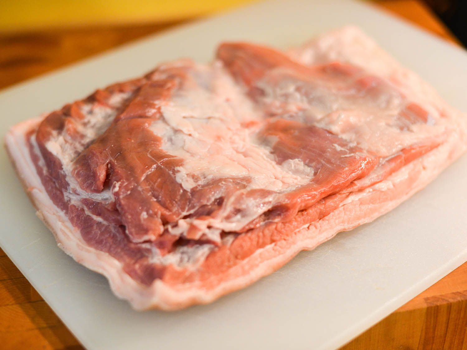 A slab of pork belly on a plastic white cutting board. 