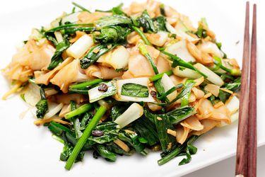 Vegan Chow Fun with bok choy, chives, and fermented beans, plated with a pair of chopsticks perched on the side