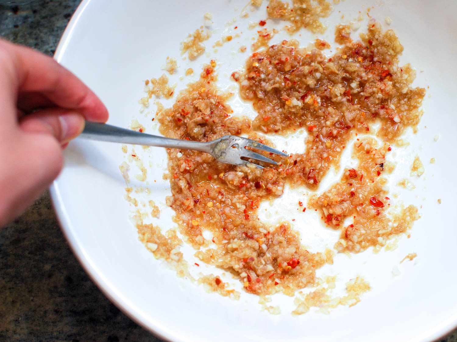 Closeup of the marinade ingredients being whisked together with a fork in a ceramic bowl.