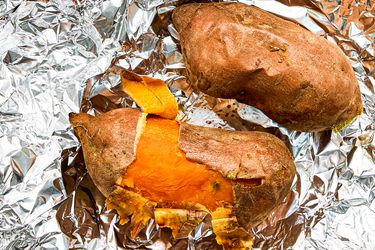 Two roasted sweet potatoes on foil one partially peeled to expose the orange flesh inside