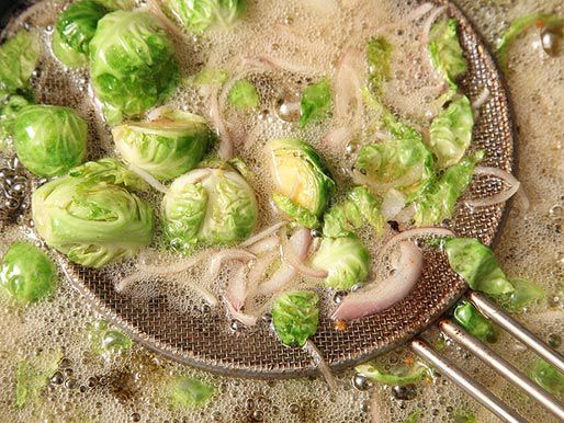 A metal spider scooping out Brussels sprouts and shallots from hot oil.