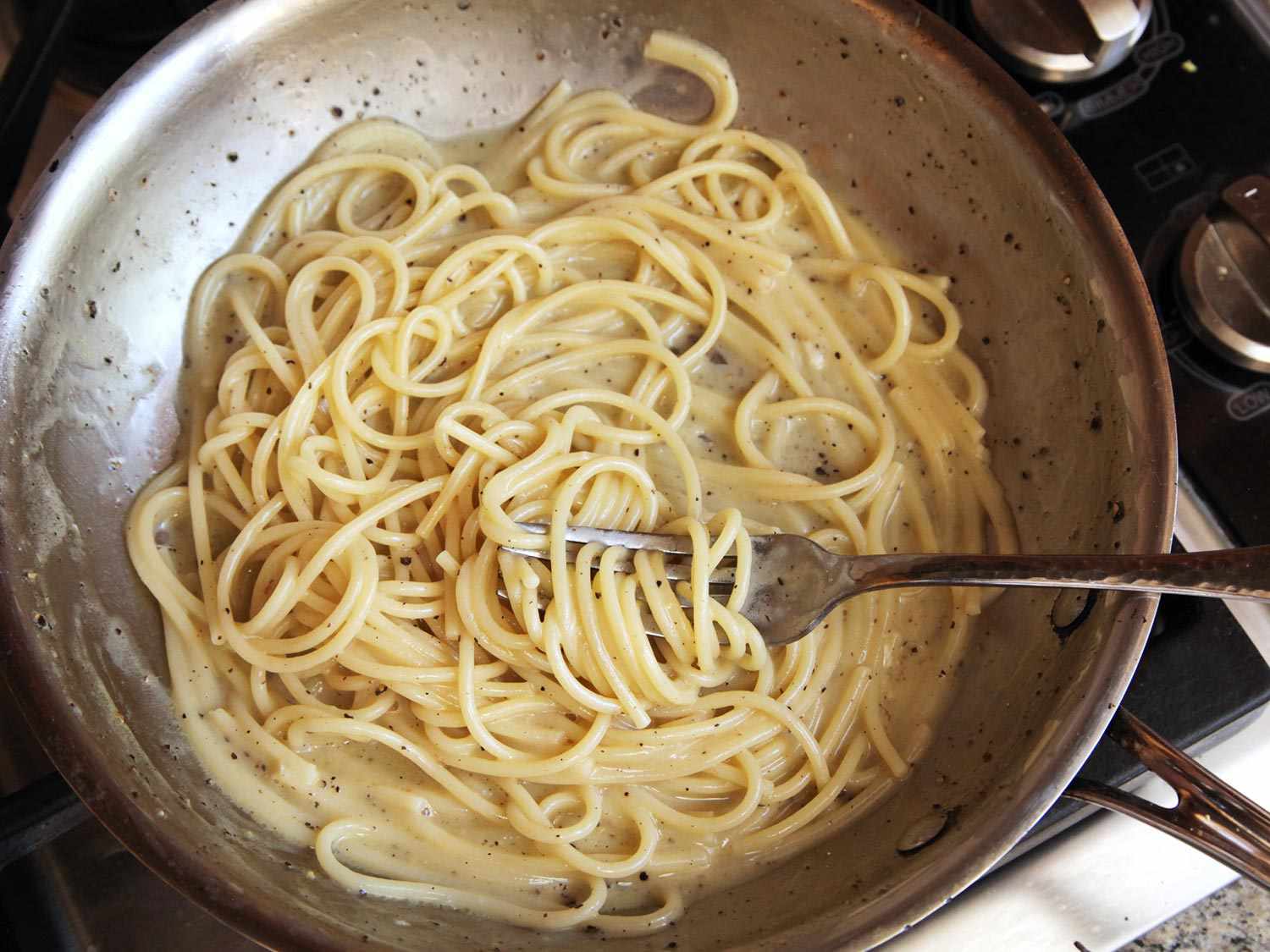 Stirring together cacio e pepe in a skillet using a fork