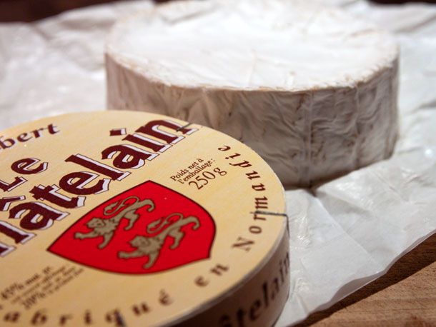 A wheel of camembert next to it's wooden packaging.