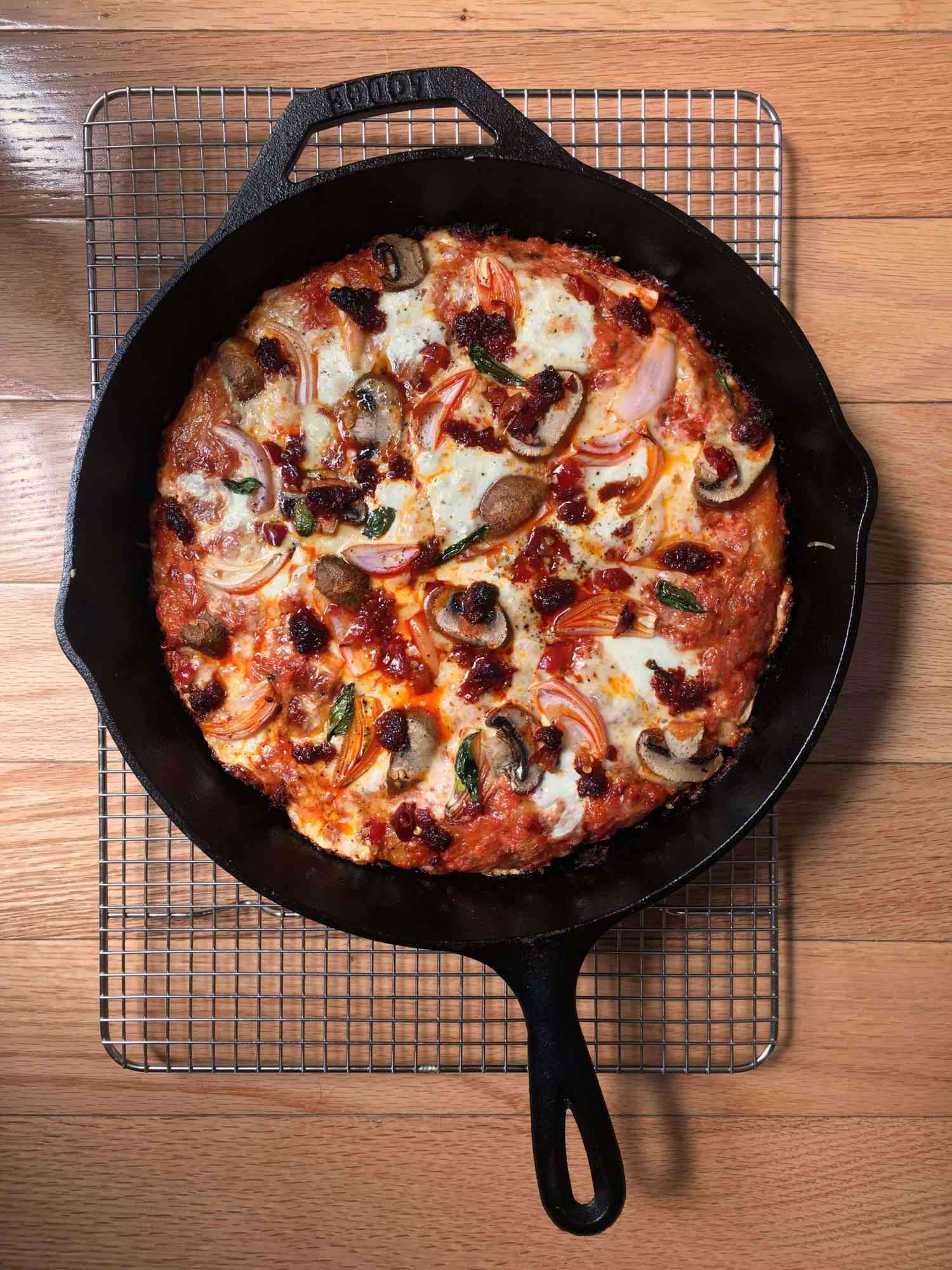 overhead view of pan pizza in a cast iron skillet resting on a wire rack