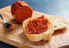 'Nduja next to a slice of bread slathered with 'nduja and a knife on a wooden block.