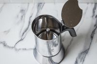 A stovetop espresso maker with its lid open placed on a marblepatterned countertop