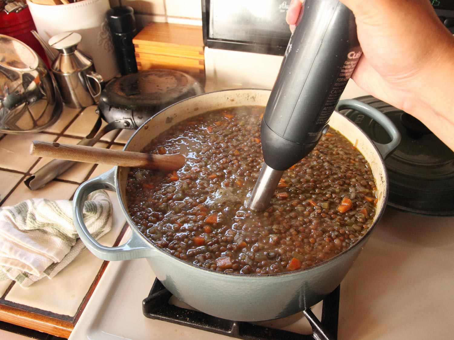 Using an immersion blender to partially blend lentil soup.