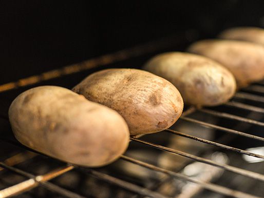 A row of russet potatoes baking on an oven rack.