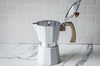 A stovetop espresso maker with an open lid and wooden handle on a marble surface