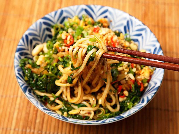 A ceramic bowl holding the composed noodles, some of which are being lifted out of the bowl by a pair of wooden chopsticks.