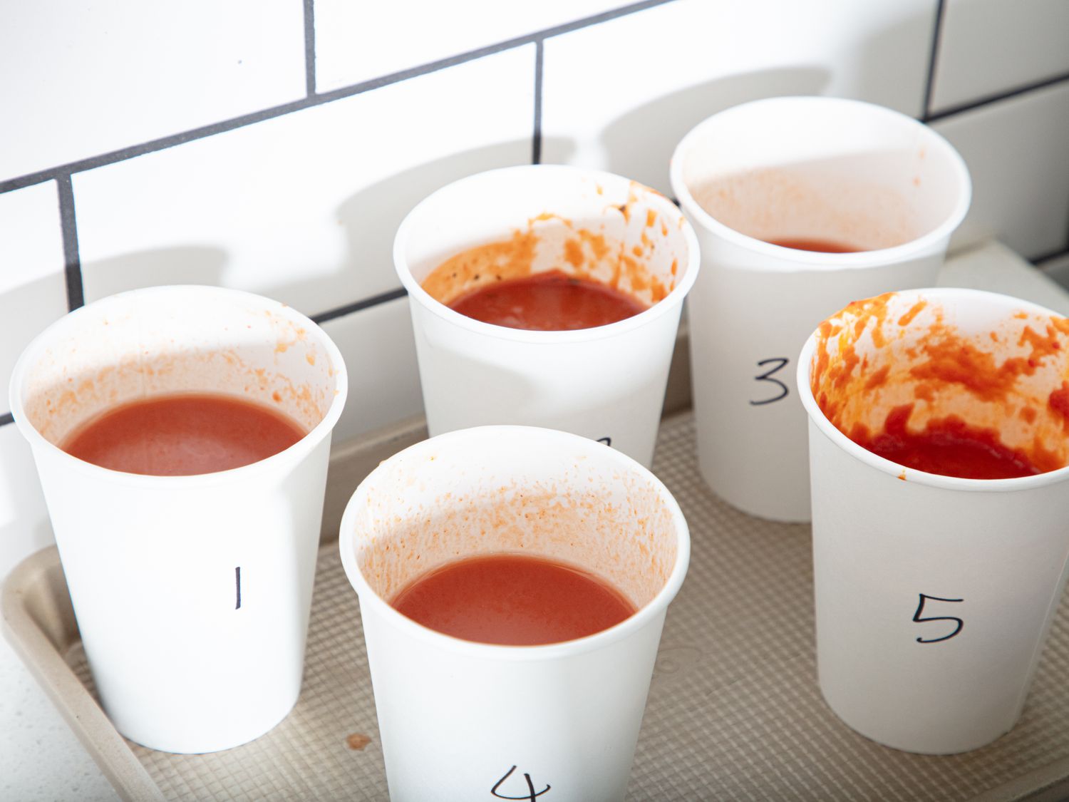 Five numbered cups containing samples of tomato soup for a taste test arranged on a tray and labeled 1 through 5