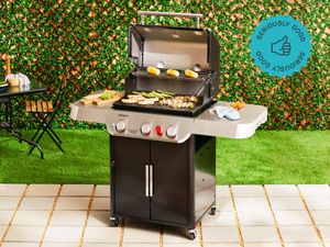 the weber genesis e-325 gas grill on a tile patio with grass behind it