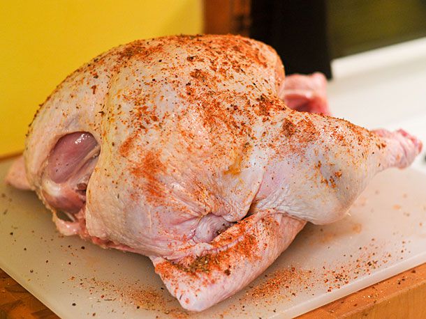 A raw turkey on a cutting board spread all over with spices.