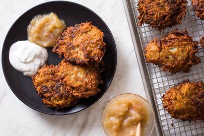 Plate of potato latkes with sour cream and applesauce additional latkes on a cooling rack