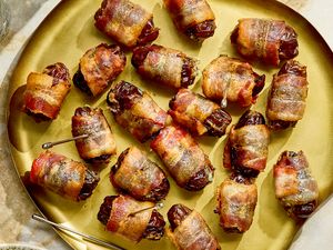 A plate of baconwrapped appetizers on a countertop served with small dishes and drink glasses