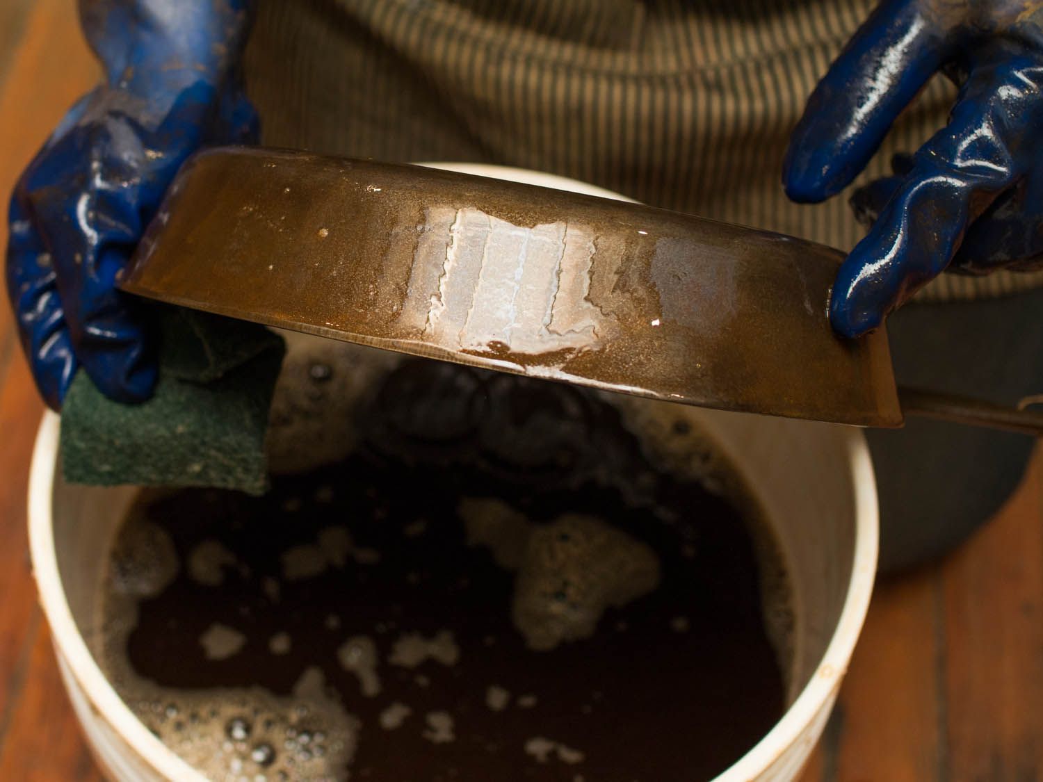 Gloved hands holding and scrubbing the side of a cast iron skillet.
