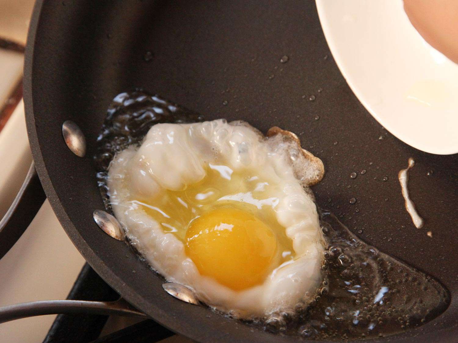 Frying eggs in a tilted pan to help maintain their shape for huevos rancheros