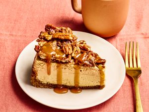 Slice of pecan pie cheesecake on a plate with a fork and mug on a table