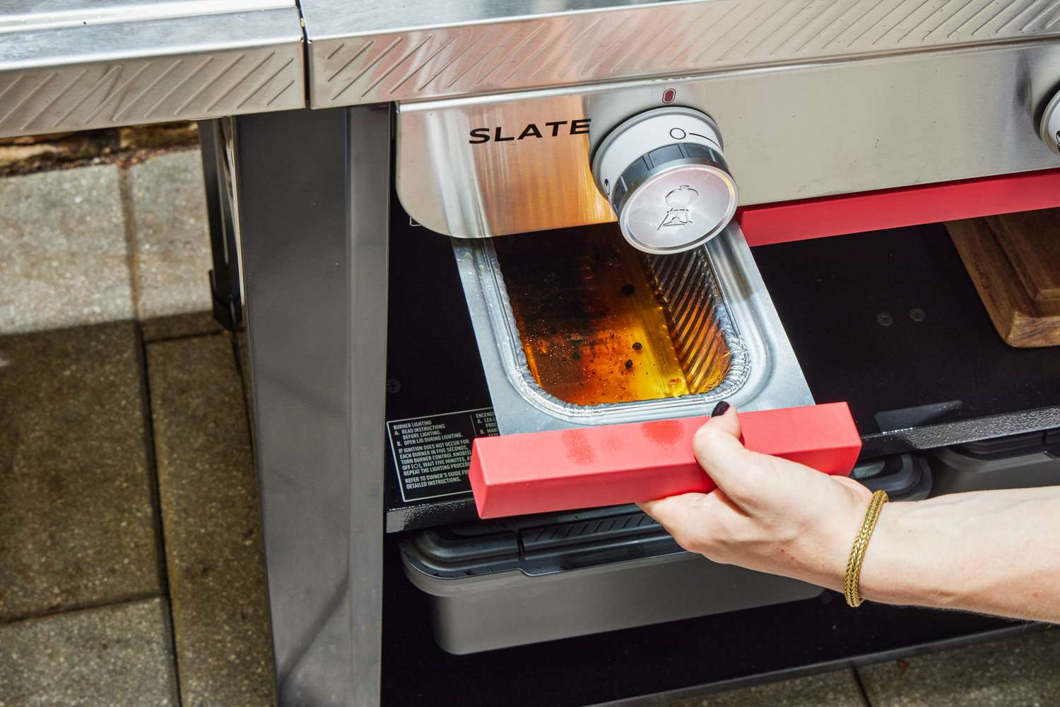 A person removes the drip tray from the Weber Slate 30 Inch Griddle