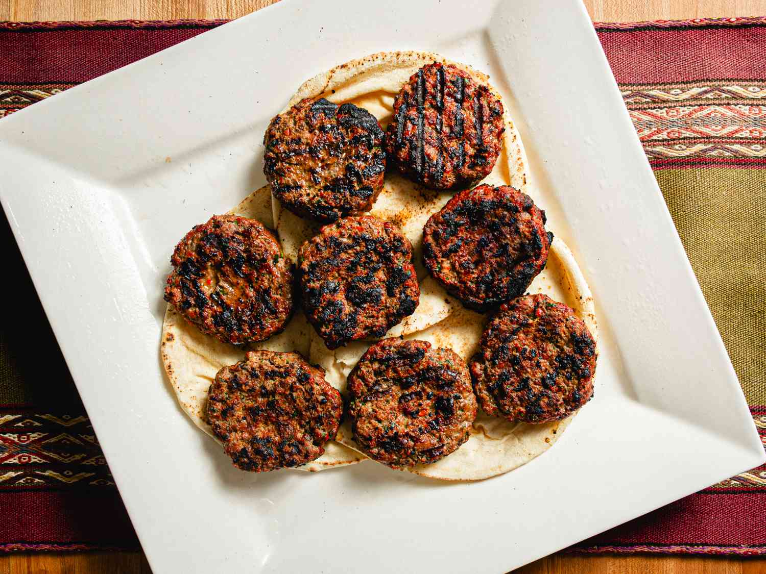 Overhead view of losh kebabs on pita on a white plate on a nicely textured, striped fabric
