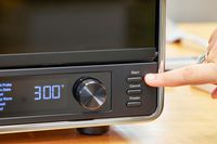 A finger pressing the start button on the KitchenAid Dual Convection Countertop Oven with Air Fryer