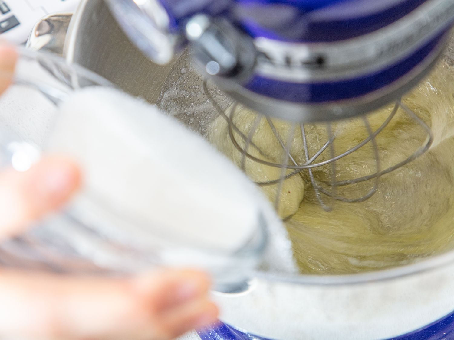 Mixing ingredients in a stand mixer with a hand adding from a small bowl