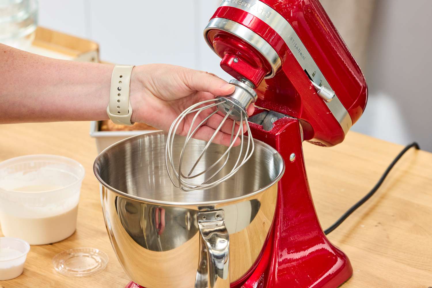 A person attaches the whisk attachment to the KitchenAid Artisan Mini 3.5-Quart Tilt-Head Stand Mixer