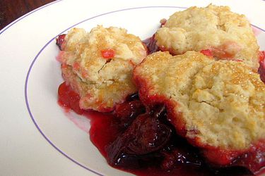 A large serving of plum and ginger cobbler plopped unto a white plate.