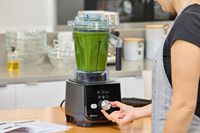 A hand touching a nob on the Vitamix Ascent X5 Blender containing green liquid