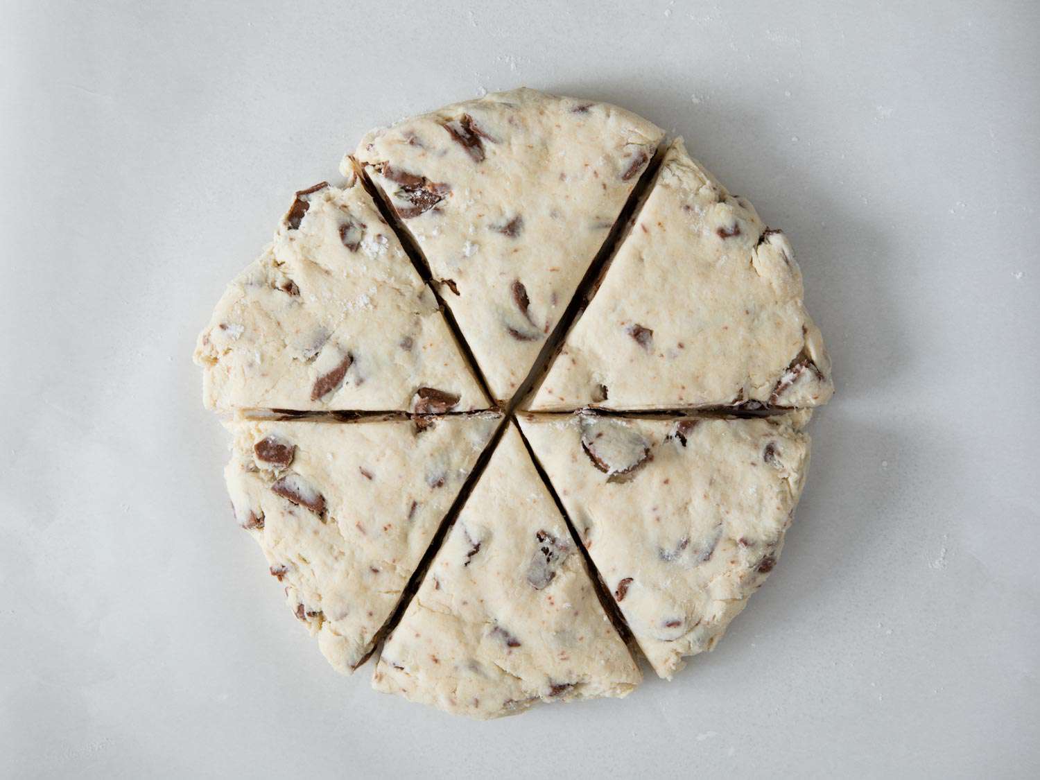 Overhead photo of a round chocolate chip scone dough cut into six wedges.