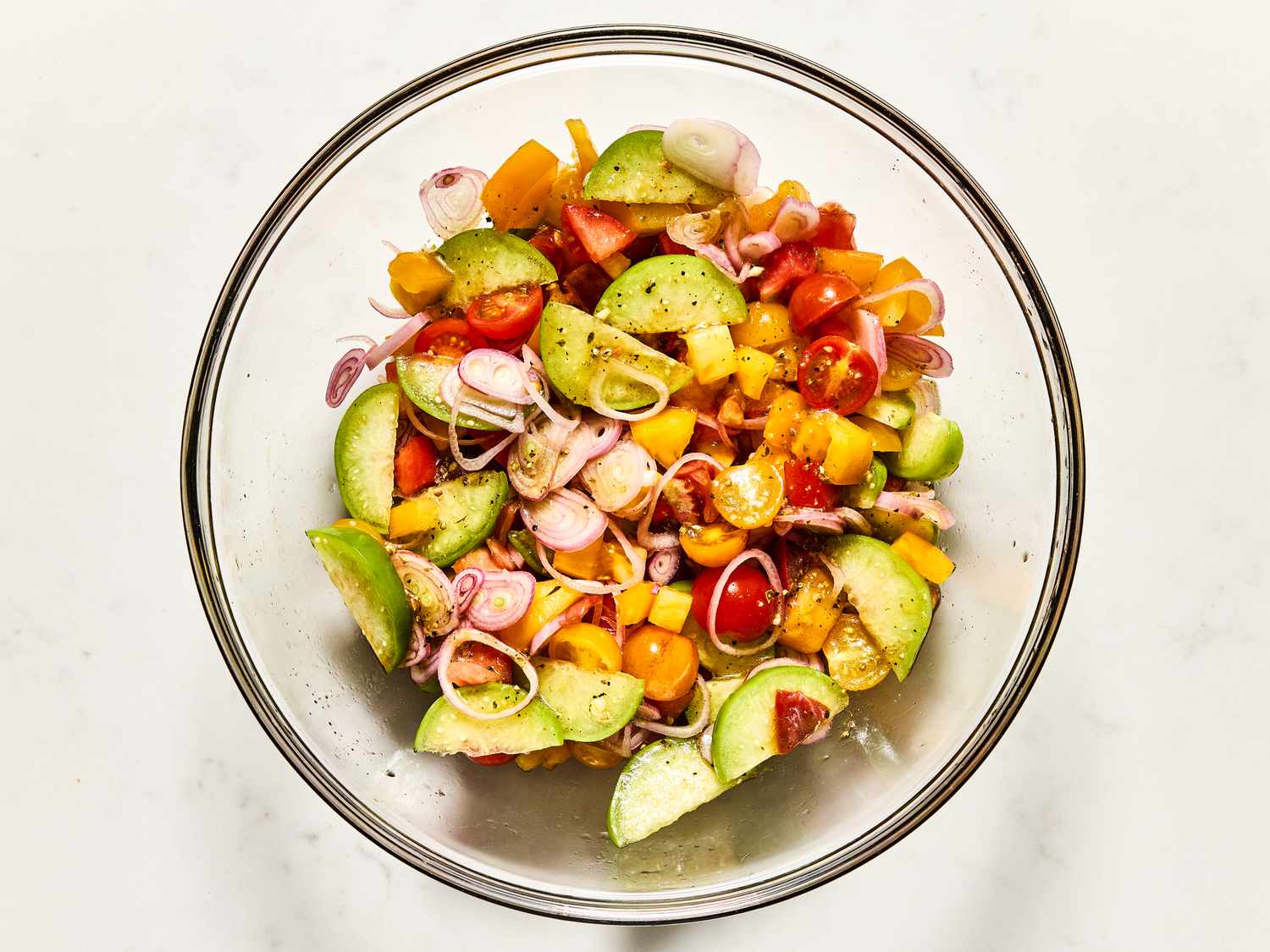 A glass bowl containing a colorful mixture of sliced vegetables and herbs, such as tomatoes and cucumbers, prepared for a salad