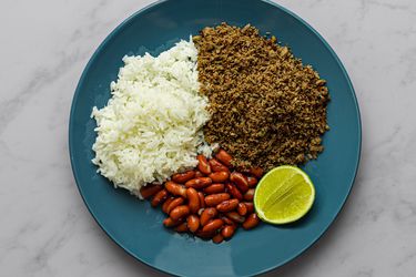 SalpicÃ³n, white rice, red kidney beans, and a slice of lime on a blue plate on a marble counter.