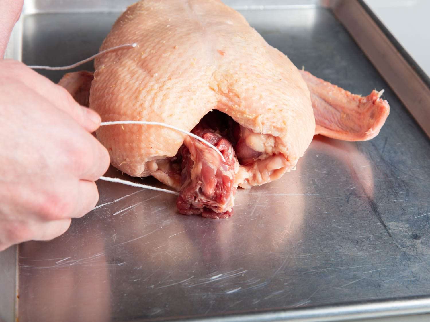 Closeup of tying a butcher's knot around the neck of a duck with twine.