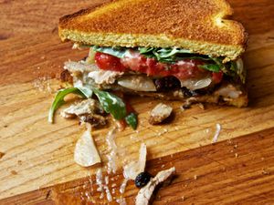 Half of a turkey club shawarma sandwich with pork belly and enhanced mayo on a cutting board. A few stray pieces of sandwich filling are strewn on the cutting board.