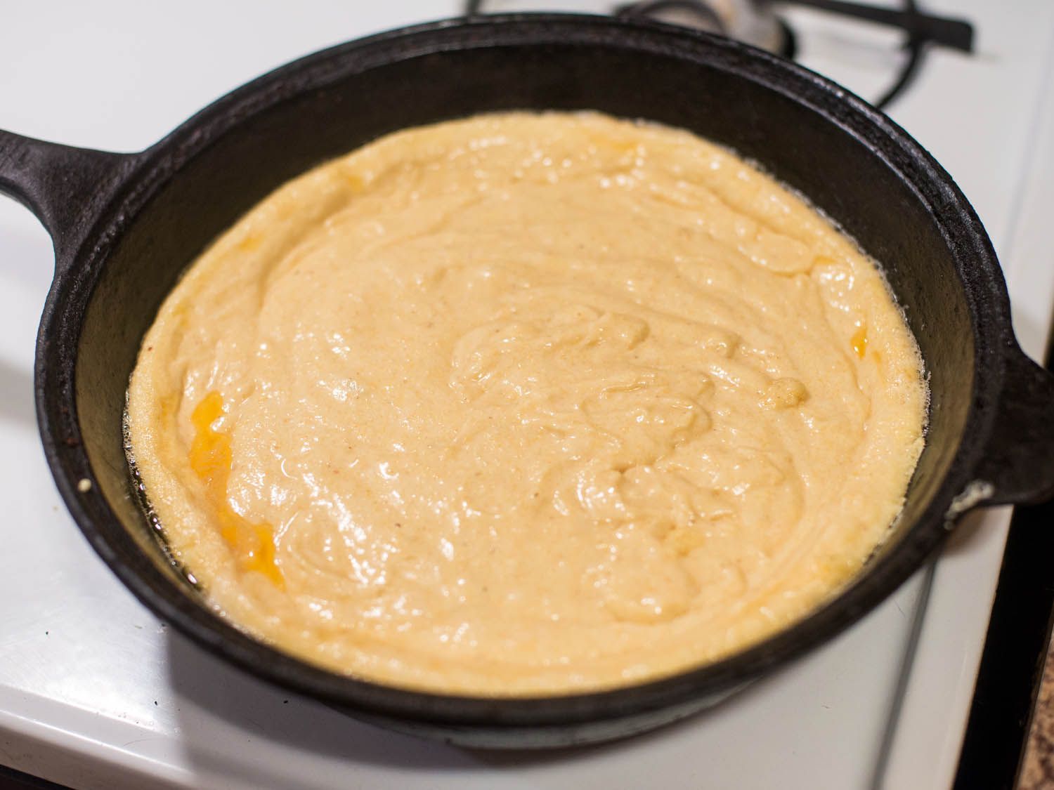 Uncooked cornbread batter in a cast iron skillet; its edge has been slightly set. 