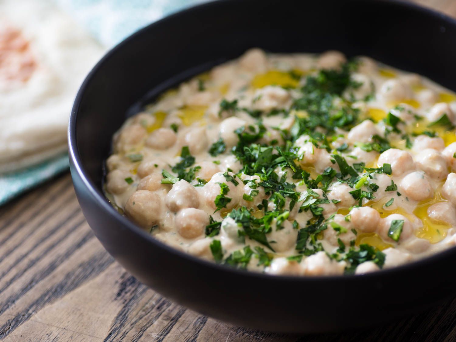 A bowl of hummus masabacha topped with chopped parsley and drizzled with olive oil