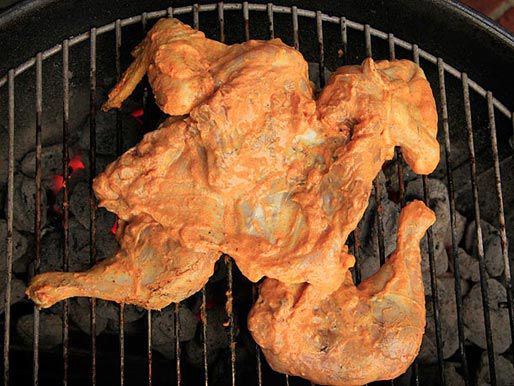 A butterflied skinless chicken with savory yogurt marinade on the grill.