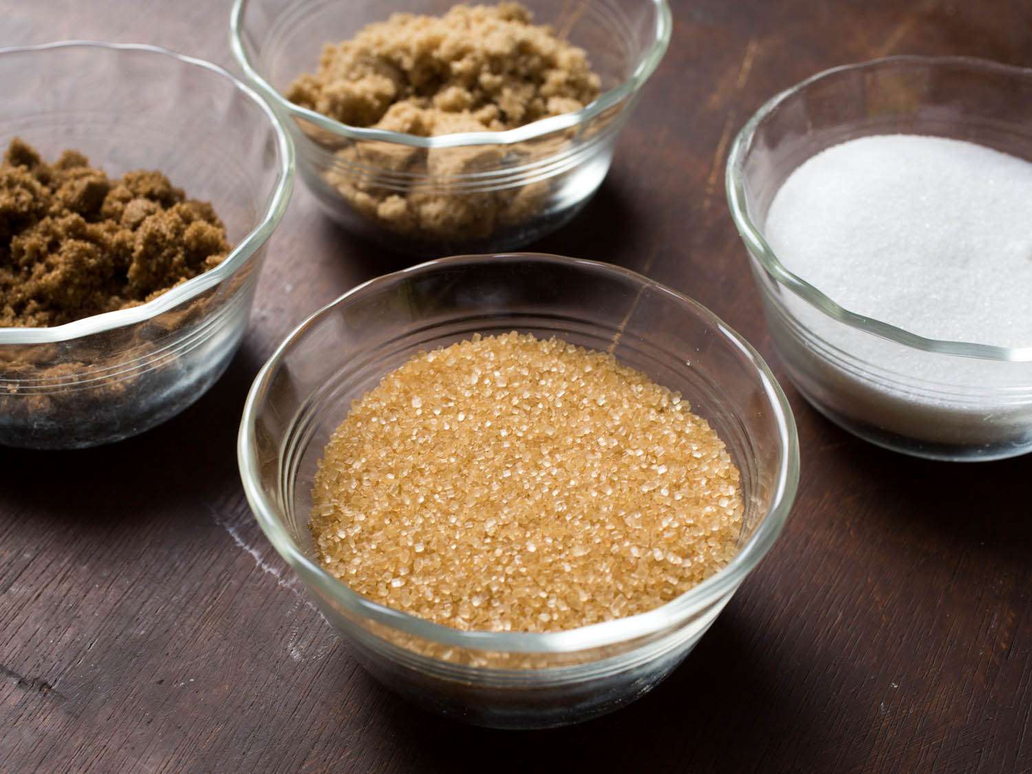 Glass bowls of various types of sugar (raw sugar, white sugar, light brown sugar, and dark brown sugar).