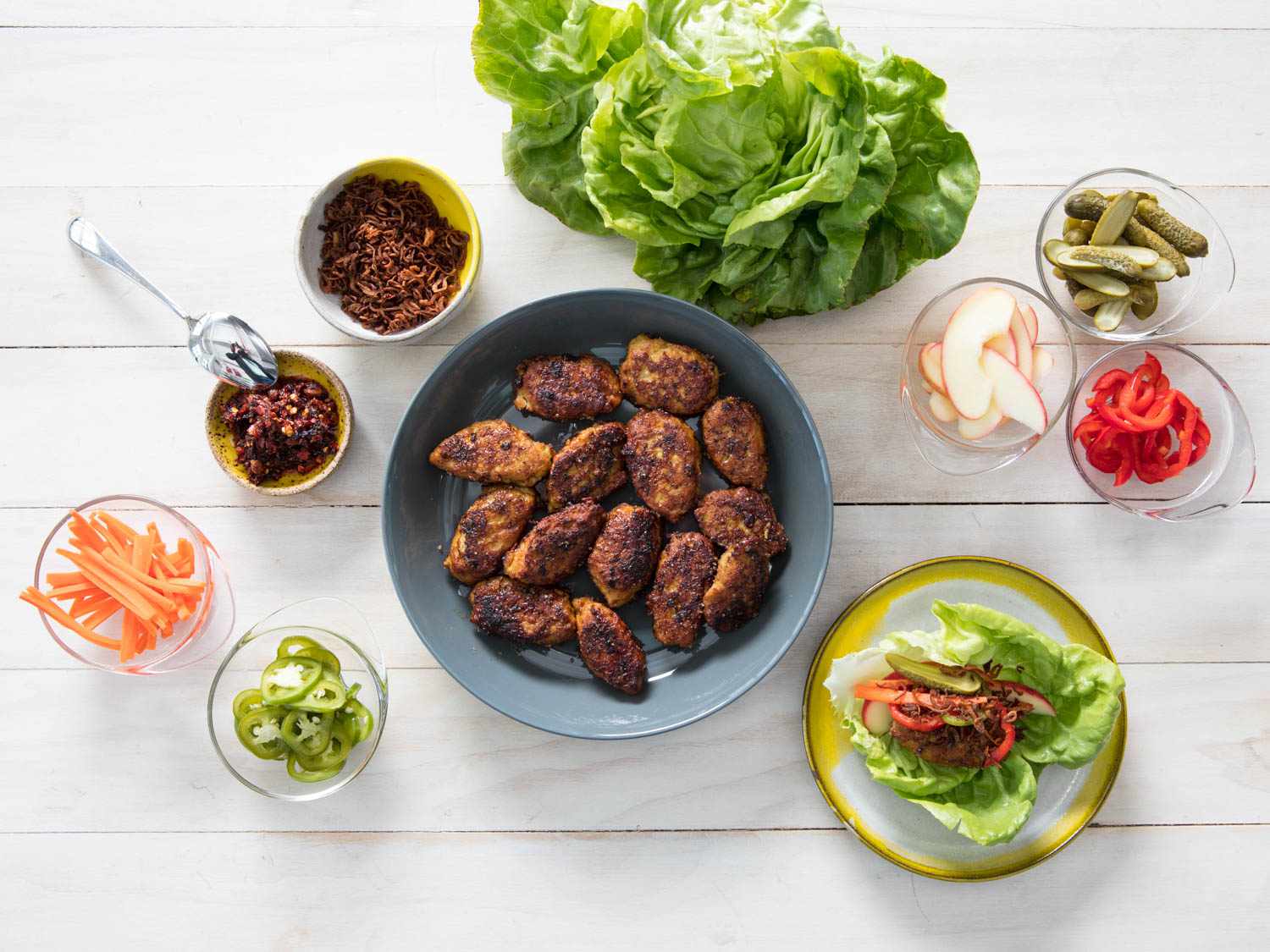 Overhead view of Vietnamese-Style Chicken Meatballs With Ginger and Mint, served on a white table with lettuce leaves, garnishes, and condiments.
