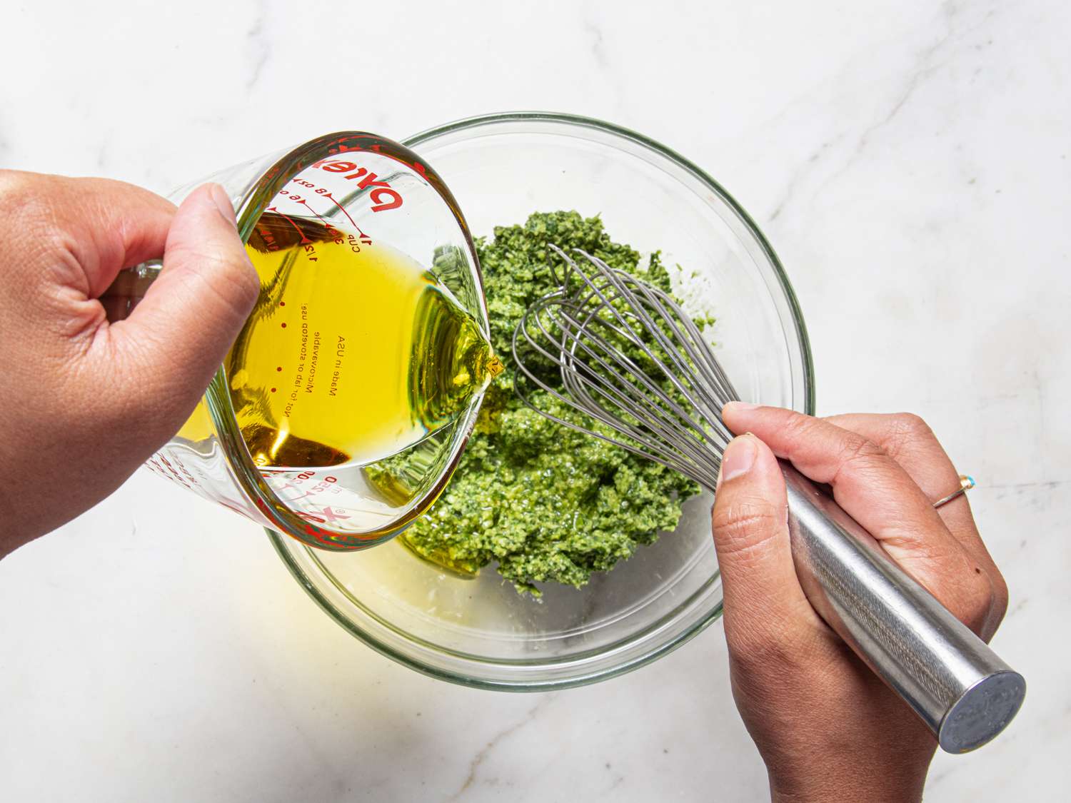 Oil being whisked into pesto base in a glass bowl