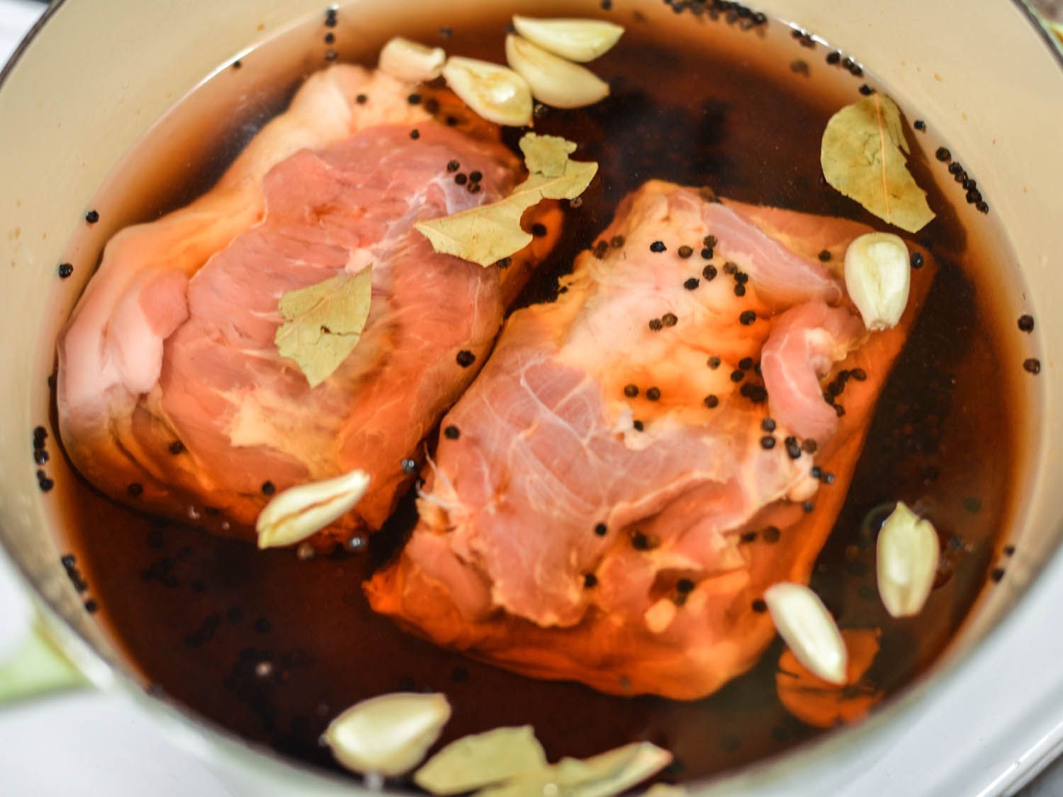 Pork belly boiled in a pot, filled with a dark liquid, seasoned with black peppercorns, garlic and bay leaves. 