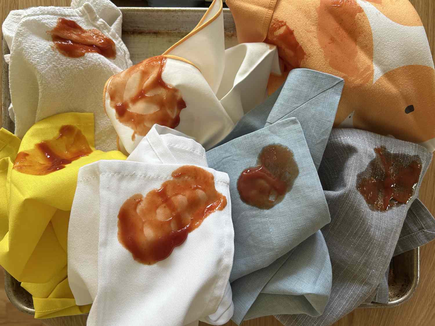 Many cloth napkins on a sheet pan, all smeared with ketchup.