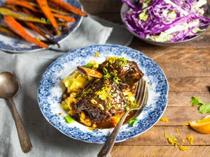 Blue and white bowl of a braised shortrib dinner with bowls of roasted carrots and cabbage in background