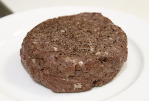 A reverse seared hamburger on a plate, which hasn't been finished in a pan and looks very gray and horrible.