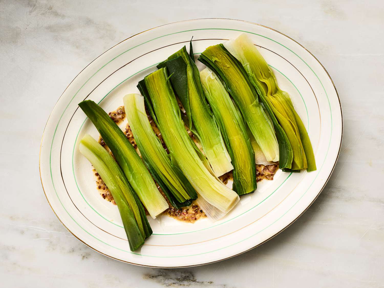 Plate of cooked leeks arranged over a grainy mustard vinaigrette
