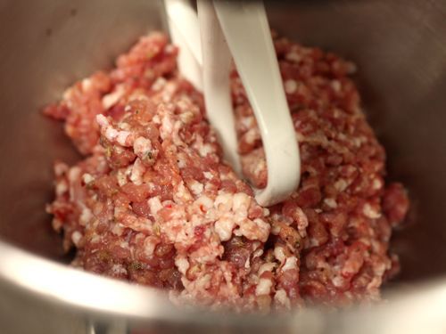 Sausage meat being kneaded with the paddle attachment in a stand mixer